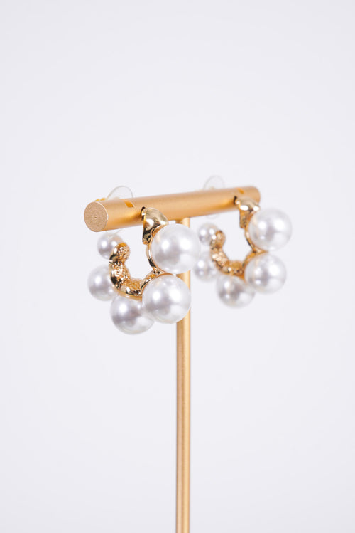 Photo shows a pair of gold mini hoops with various sizes of pearls on the outside of the hoop. 