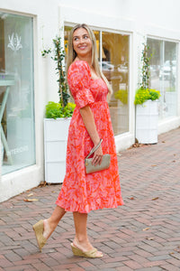 model is wearing a pink midi dress with puff sleeves, paired with a gold wristlet and wedges