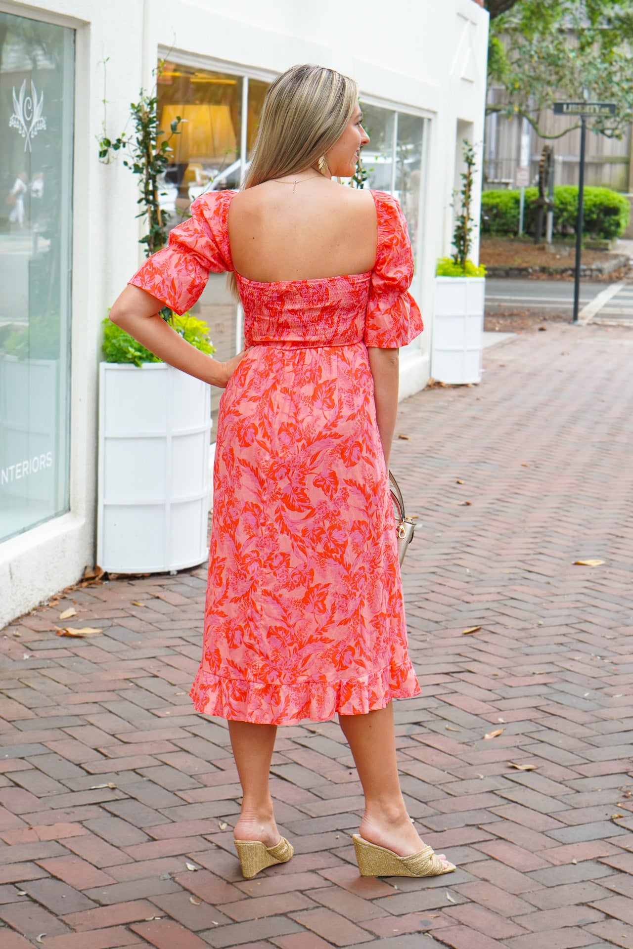model is wearing a pink midi dress with puff sleeves, paired with a gold wristlet and wedges