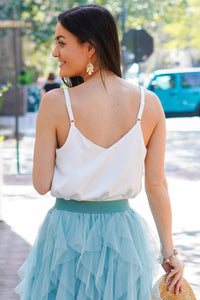 model is wearing a white satin tank paired with a blue tulle skirt and a tan sun hat.